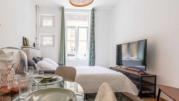 A hotel room with a bed, a TV, a dining table with plates and glasses, a chair, and a window with curtains. - Rock in Share - Le Grain de Sable (Thionville)