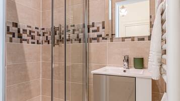 A modern bathroom with a glass shower enclosure, a white sink, and a mirror above it.