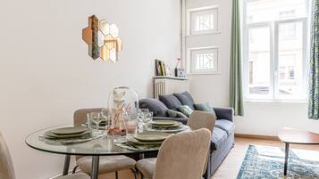 A dining area with a glass table set for four, a sofa with cushions, and a view of the street through a window.