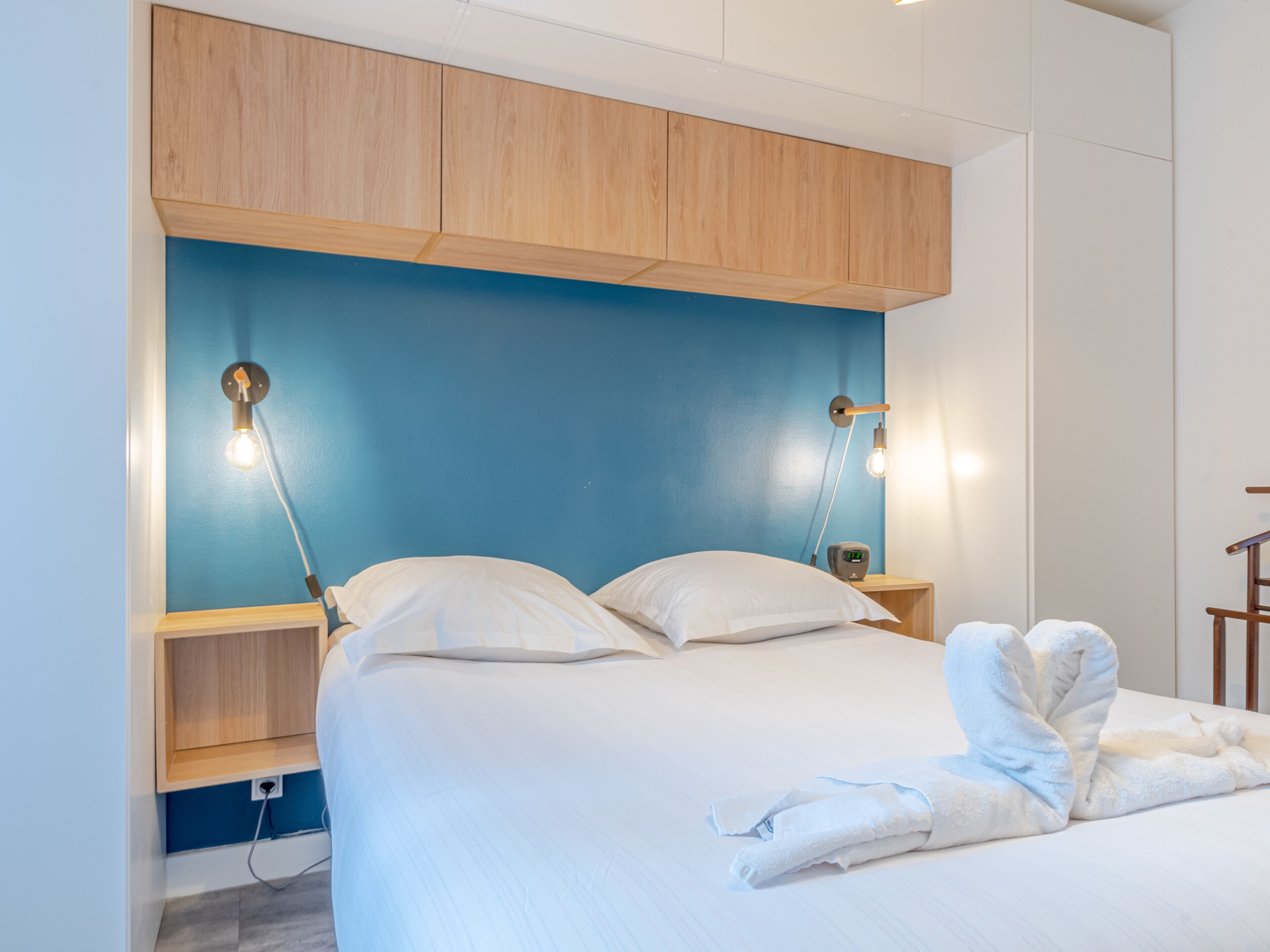 Une chambre à coucher comprenant un lit, des tables de chevet, une tête de lit en bois et des lampes fixées au mur.