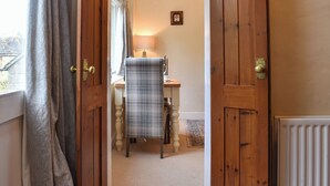A hallway with wooden doors, a table with a plaid tablecloth, a lamp, and a small framed picture on the wall.