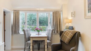 A cozy room with a dining table, two chairs, a sofa, and a window with curtains.