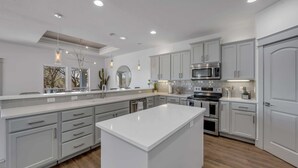 A modern kitchen with white cabinetry, a central island, stainless steel appliances, and pendant lighting.
