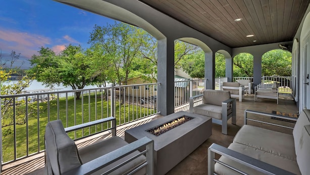 A covered outdoor patio with a fire feature, seating, and a view of a lake.