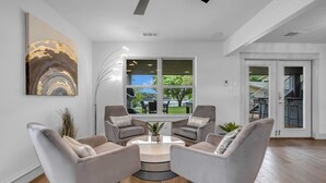A modern living room with a round coffee table, two grey armchairs, a floor lamp, and a large abstract painting on the wall.