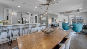 A modern kitchen with a central island, bar stools, a dining table, and a living area with a sofa and chairs.