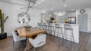 A modern kitchen with white cabinets, a central island with bar stools, and a dining area with a wooden table and chairs.