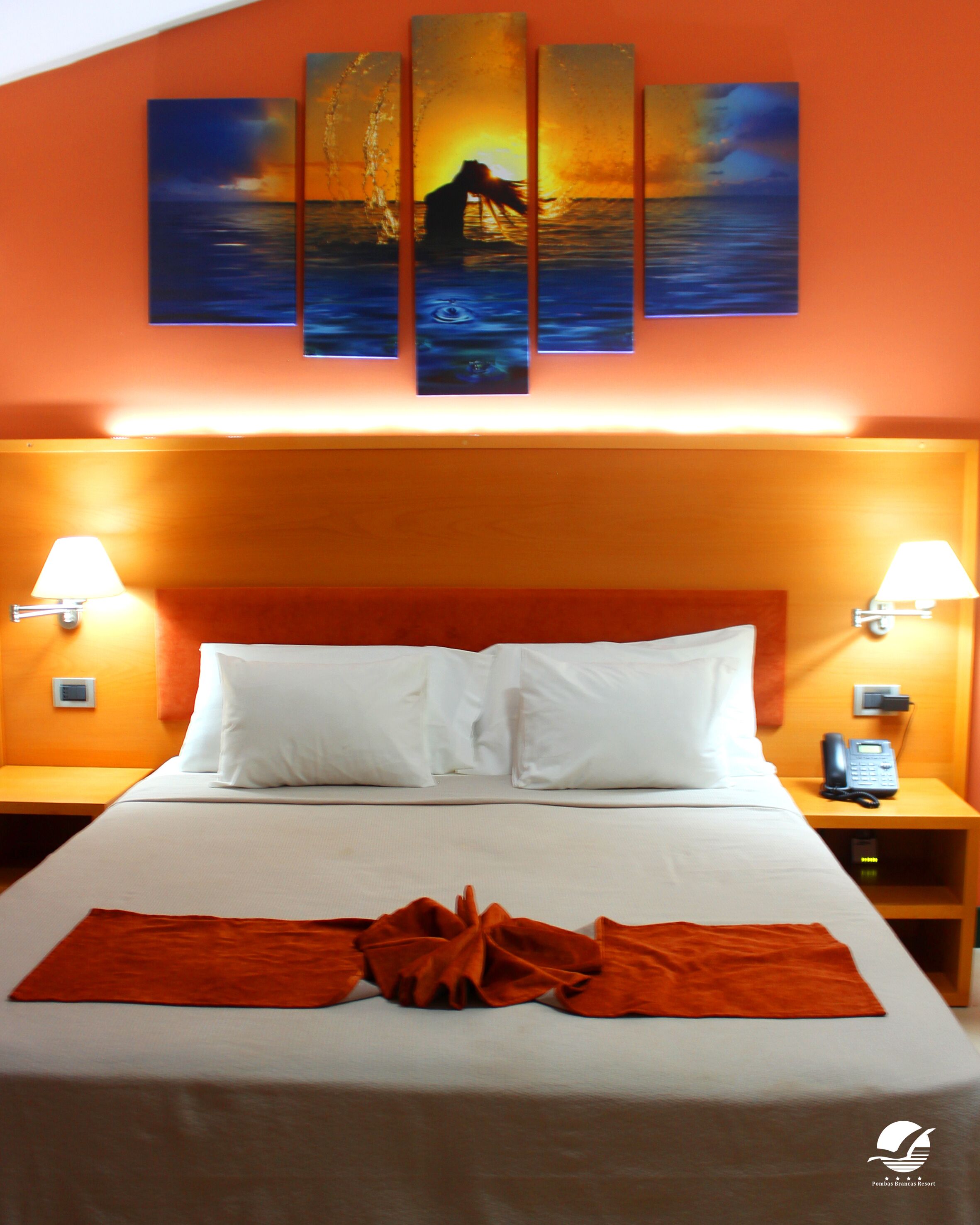 A hotel room with a large bed, white bedding, and a sunset painting on the wall.