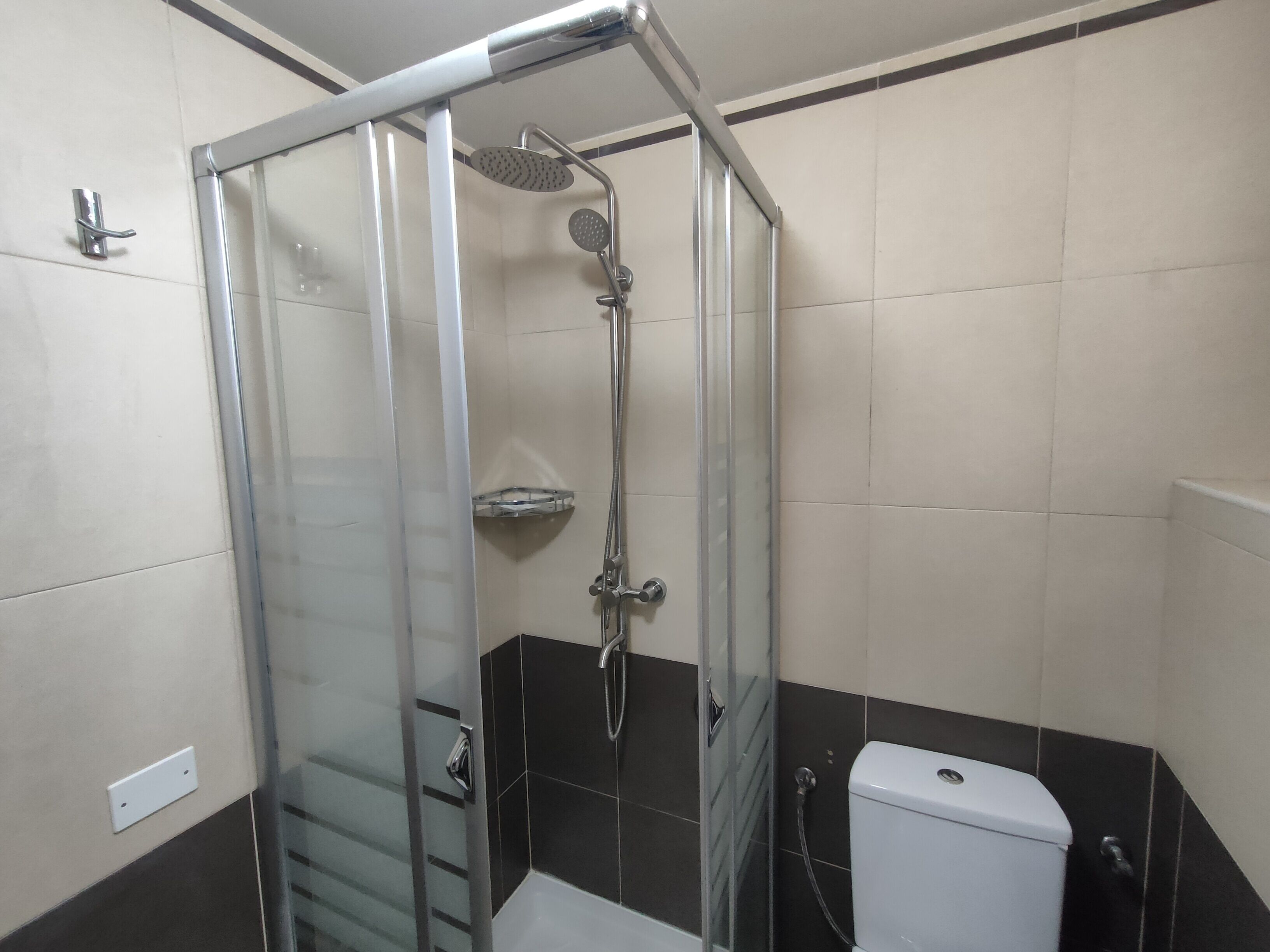 A glass-enclosed shower stall with a handheld showerhead and a wall-mounted faucet.