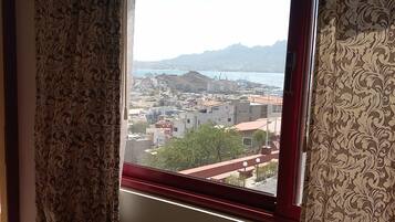 Una ventana con cortinas estampadas, vista a un paisaje urbano con edificios y montañas al fondo.