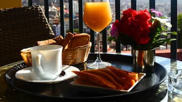Ein Frühstücksbrett mit Brot, einer Tasse Kaffee, einem Glas Orangensaft und einer Fruchtplatte, auf einem Tisch mit Bergblick.