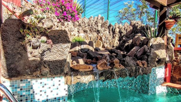 Una piscina con agua cristalina, una pared de roca y un puente de madera.