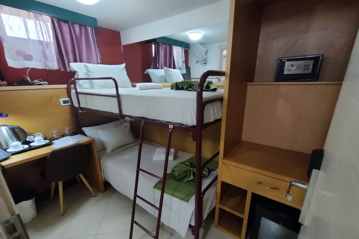 A bunk bed room with a desk, a small refrigerator, and a window with curtains.