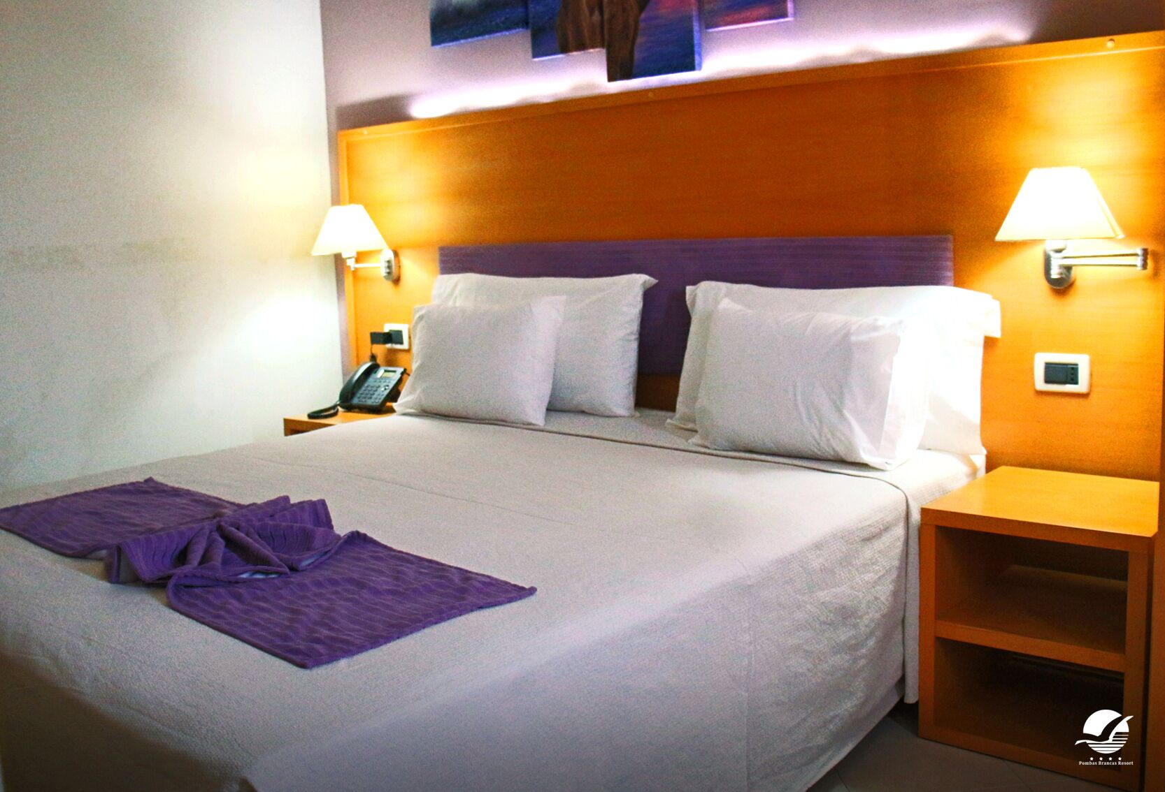 A hotel room with a large bed, two bedside tables, a phone, and a lamp on each side.
