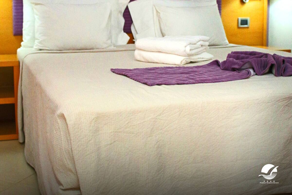 A hotel room with a large bed, a nightstand, a lamp, and a painting of a sunset over the ocean.