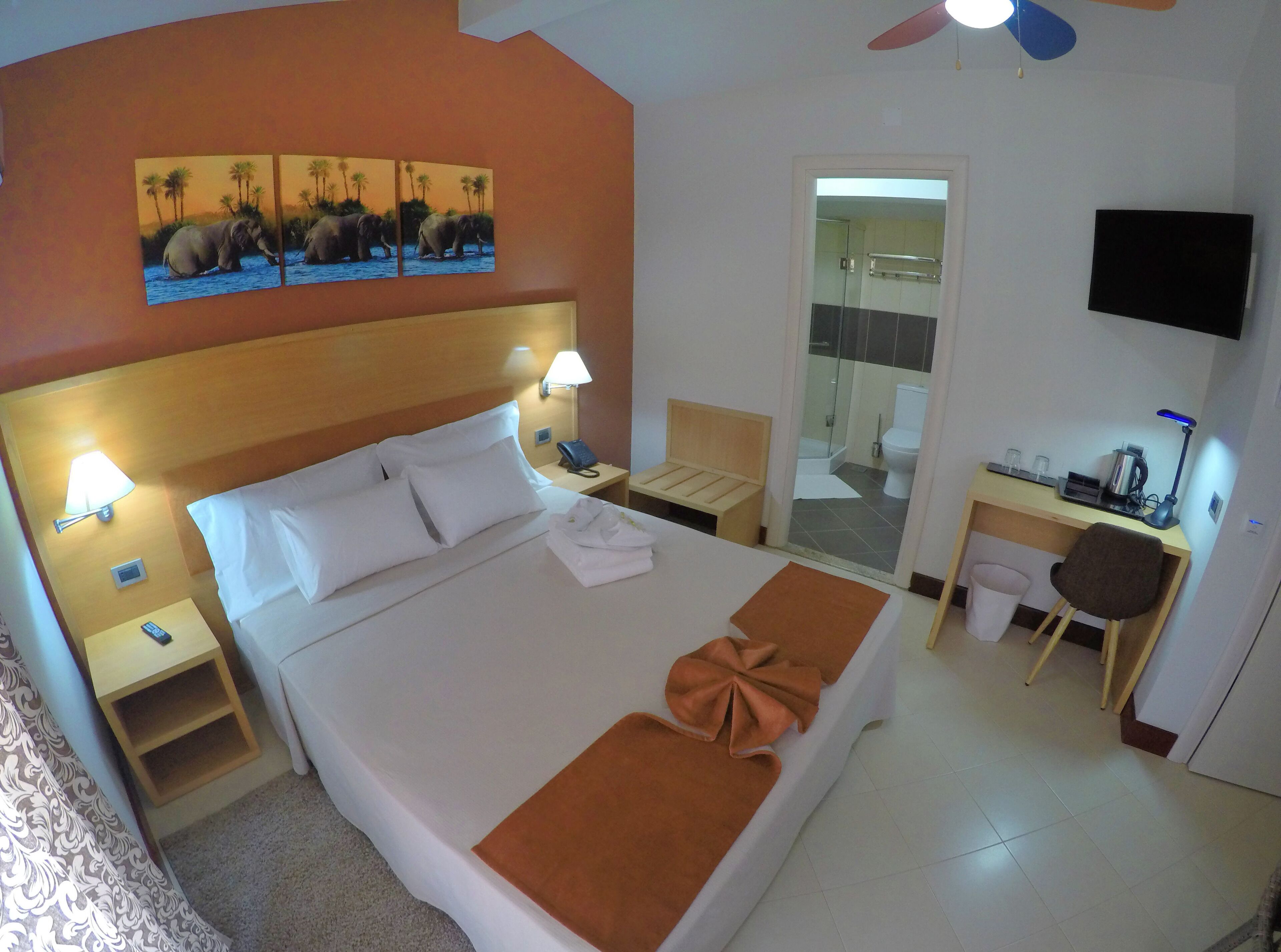 Een hotelkamer met een groot bed, een bureau, een stoel, een televisie en een badkamer zichtbaar door een glazen deur.