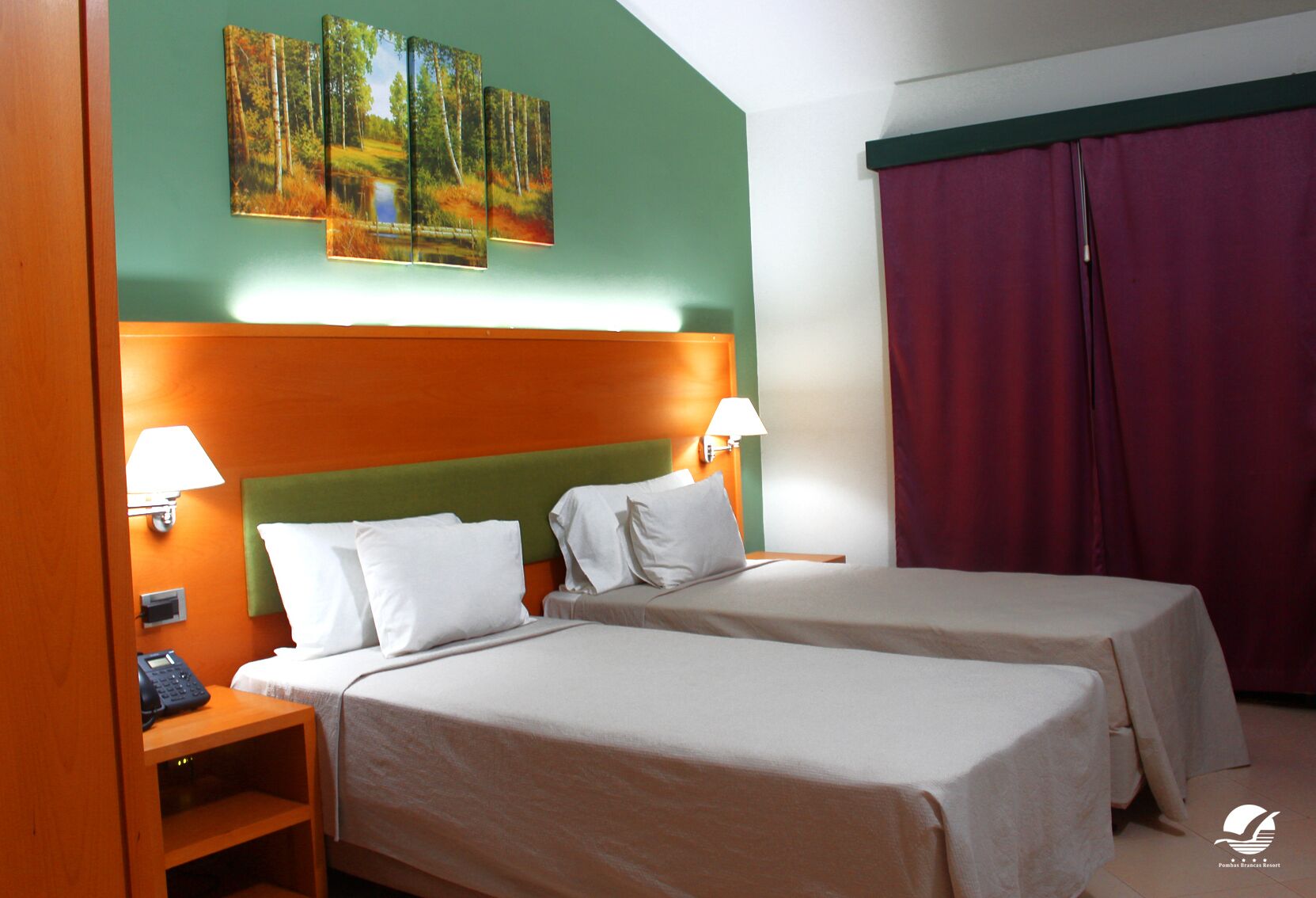 A hotel room with two beds, a green headboard, a painting of a forest, a telephone, and a red curtain.