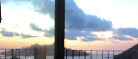 Una taza blanca con un logo sobre un platito, sobre una mesa con vista a un atardecer y nubes.