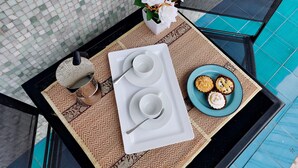 Ein Tisch mit einer Tablett voller weißer Tassen und Untertassen, einem Teller mit Cupcakes und einer Vase mit weißen Blumen.