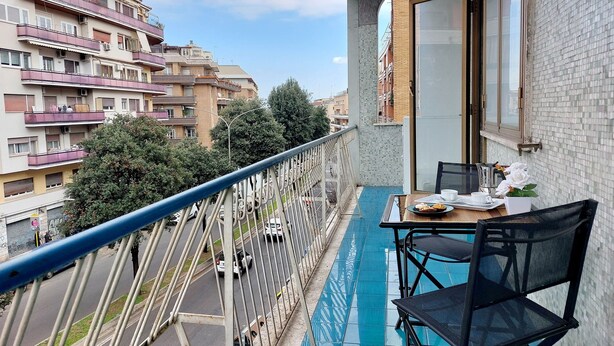Ein Balkon mit Tisch und Stühlen, Blick auf die Straße und ein Gebäude mit Balkonen.