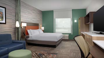 A hotel room with a bed, a desk, a chair, a sofa, and a television.