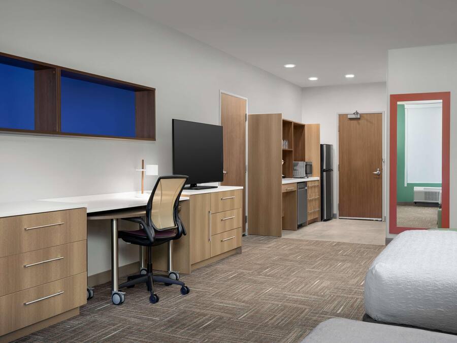 A modern hotel room with a desk, chair, wardrobe, and a bed.