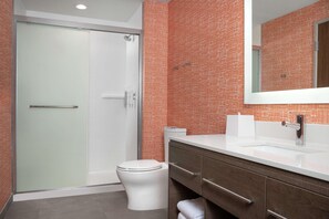 A modern bathroom with a glass shower enclosure, a white toilet, and a wooden vanity with a mirror. - Home2 Suites By Hilton Cullman (Cullman)