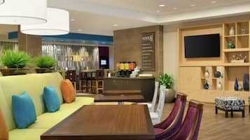 Un moderno vestíbulo de hotel con un sofá, una mesa de comedor, sillas, una zona de bar y un televisor en la pared.