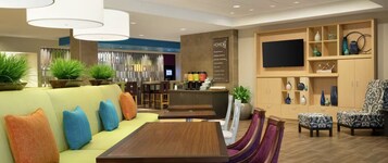 Un moderno vestíbulo de hotel con un sofá, una mesa de comedor, sillas, una zona de bar y un televisor en la pared.