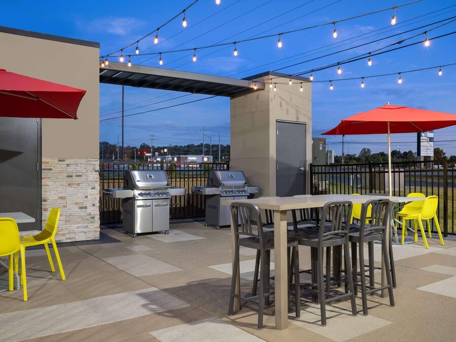 Un espace extérieur aménagé en terrasse, avec des barbecues, des parasols jaunes et rouges, et une vue sur les environs.