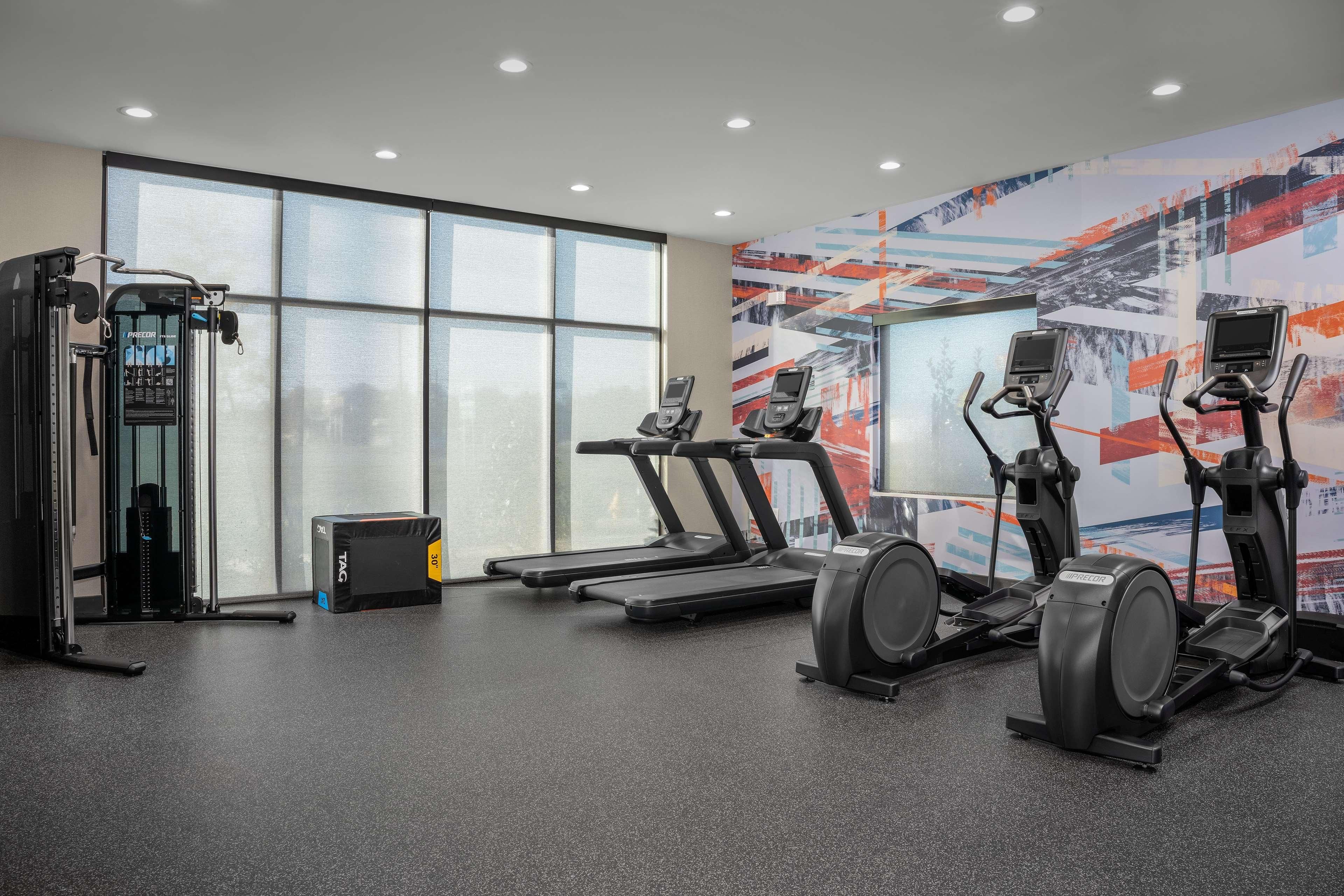 Une salle de sport équipée de tapis de course, de vélos elliptiques et d’une machine de musculation.
