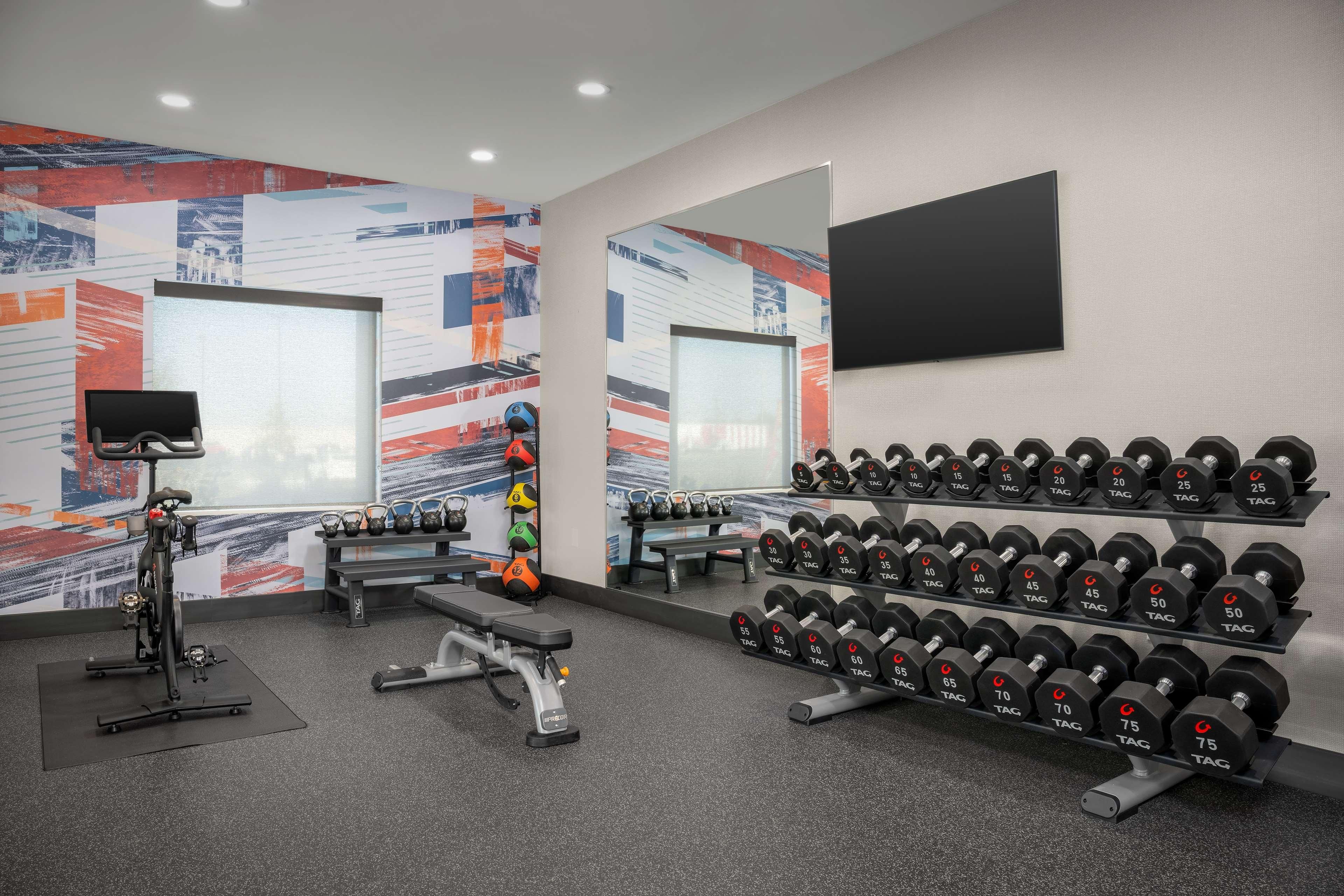 A gym with a stationary bike, dumbbells, and benches.