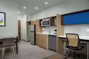 A compact kitchen with a microwave, refrigerator, and sink. There is a dining table with chairs and a small office chair.