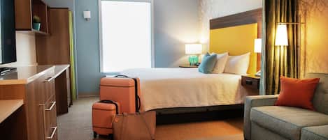 Una habitación de hotel con cama, escritorio, silla, maleta y lámpara.
