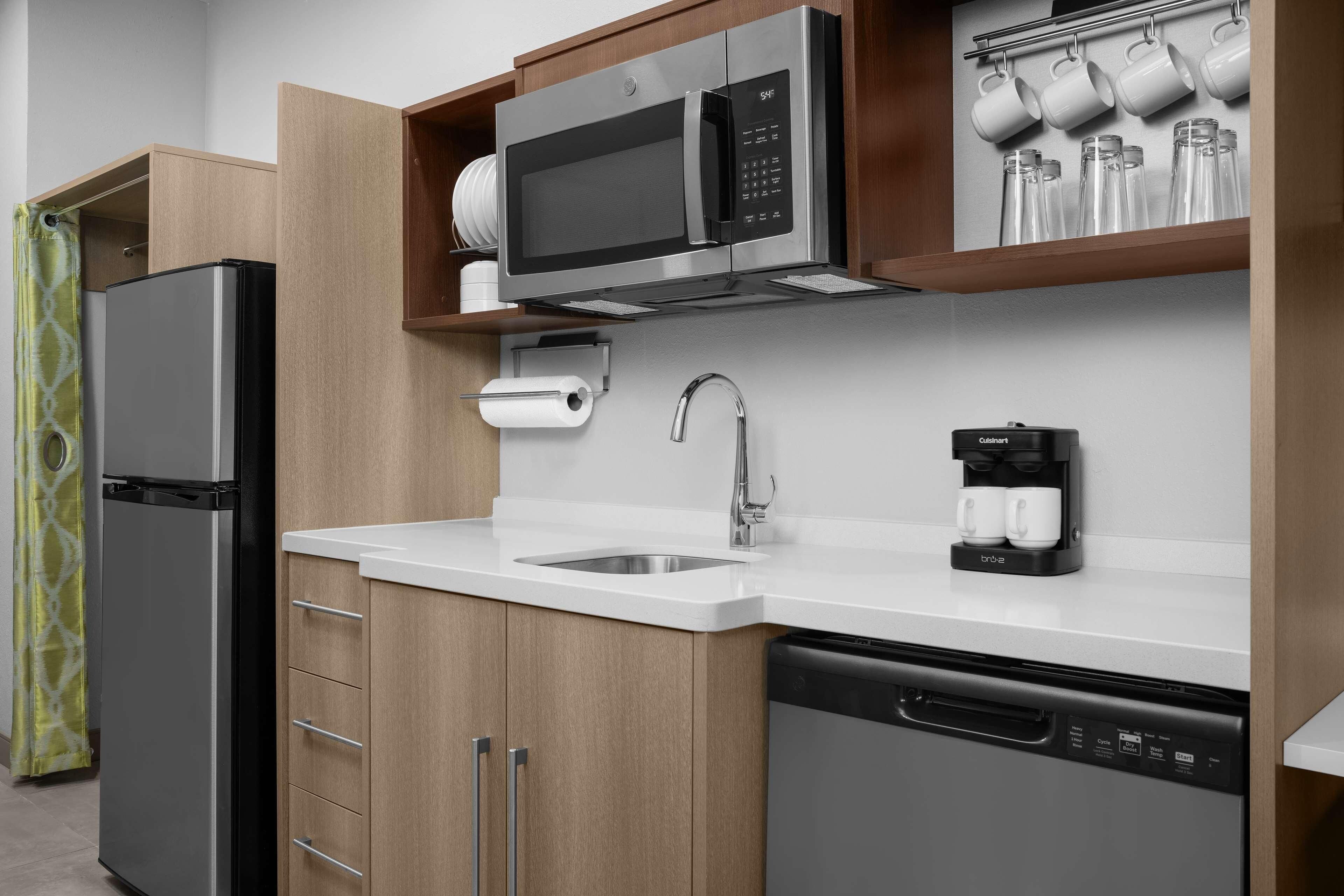 Una cocina moderna con un refrigerador de acero inoxidable, un microondas integrado, una cafetera y un lavavajillas.