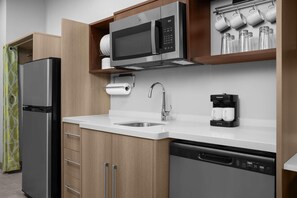 A modern kitchen with a stainless steel refrigerator, a built-in microwave, a coffee maker, and a dishwasher. - Home2 Suites By Hilton Cullman (Cullman)