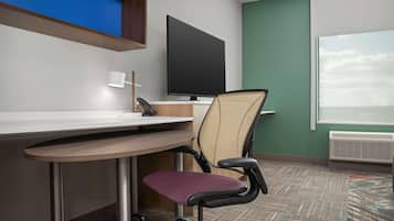 A hotel room with a desk, chair, television, and a window with blinds.