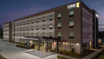 A modern hotel with a "HOME 2" sign, multiple floors, and a covered outdoor area with seating.