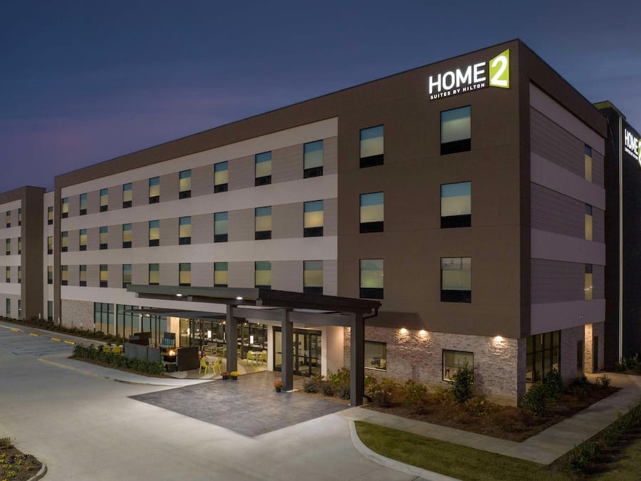 A modern hotel with a "HOME 2" sign, multiple floors, and a covered outdoor area with seating.