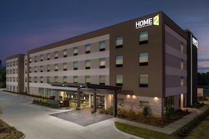 Un hotel moderno con un letrero que dice "HOME 2", varios pisos y un área exterior cubierta con asientos.