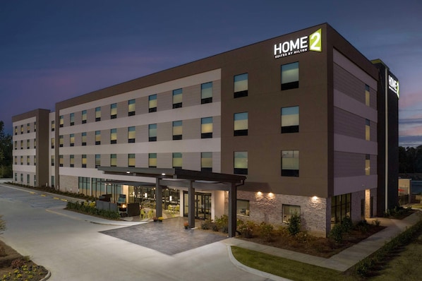A modern hotel with a "HOME 2" sign, multiple floors, and a covered outdoor area with seating. - Home2 Suites By Hilton Cullman (Cullman)