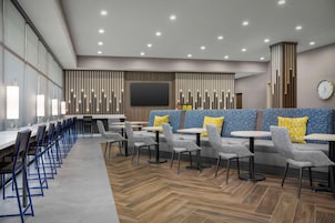 A modern restaurant with long tables and booths, a large TV screen, and a clock on the wall.