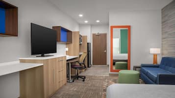 A modern hotel room with a flat-screen TV, a desk with a chair, a sofa, and a small table with a lamp.