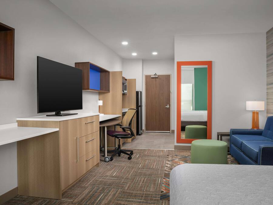 A modern hotel room with a flat-screen TV, a desk with a chair, a sofa, and a small table with a lamp.
