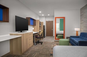 Habitación de hotel moderna con televisión de pantalla plana, un escritorio con silla, un sofá y una mesita con lámpara.