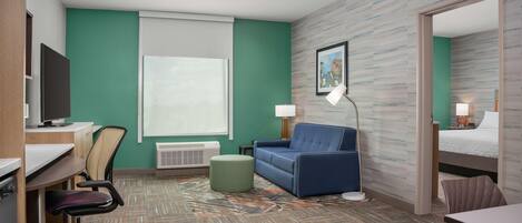 Une chambre d’hôtel équipée d’un bureau, d’une chaise, d’un canapé, d’un pouf et d’un lit.