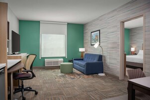 A hotel room with a desk, chair, sofa, ottoman, and a bed.