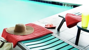 Zona de piscina con una silla de descanso, una toalla roja, un sombrero de paja, chanclas y una botella amarilla.