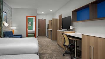 Quarto de hotel com cama, escrivaninha, cadeira, televisão e banheiro.