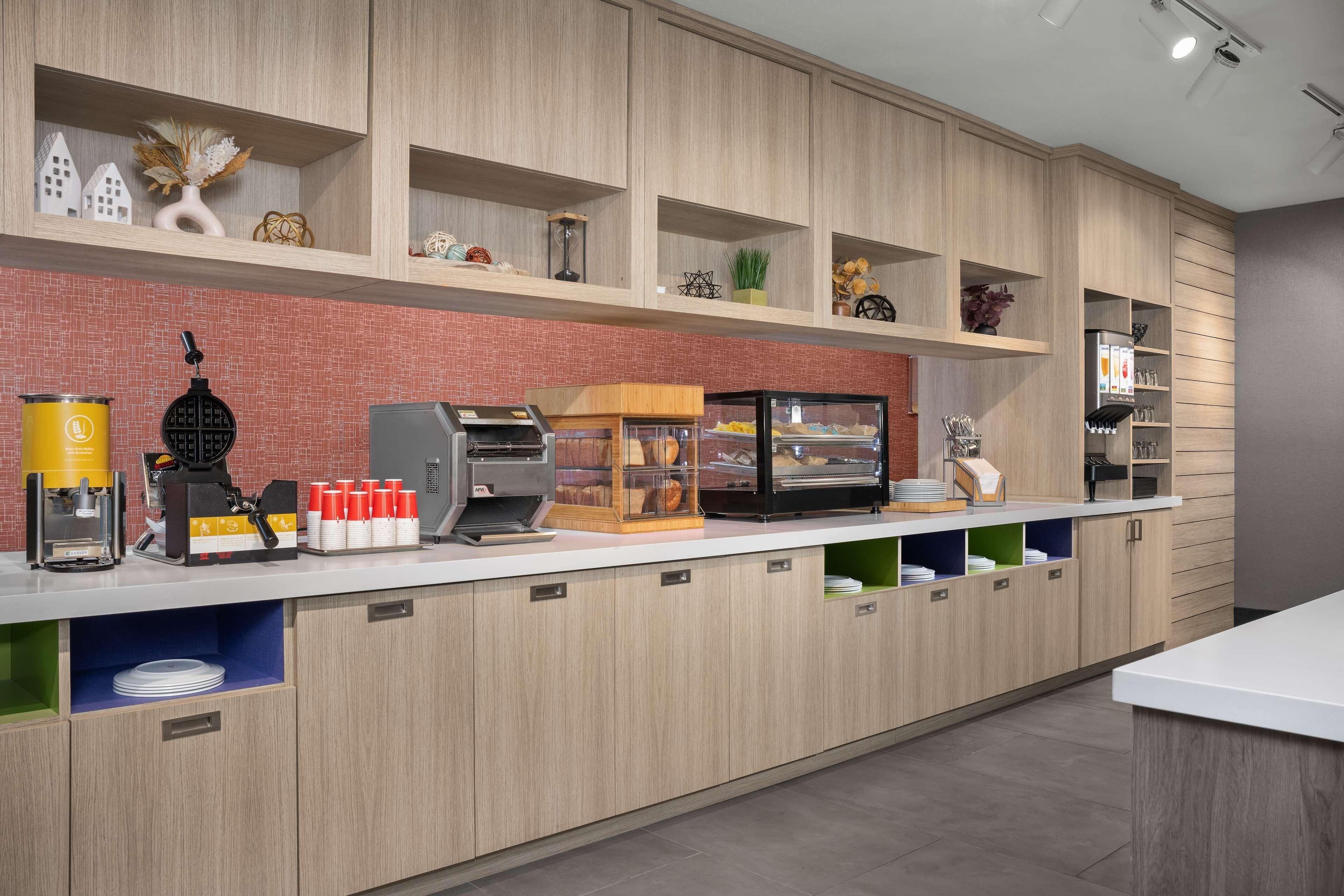 Cozinha moderna com armários de madeira, máquina de café, exposição de pão e diversos utensílios de cozinha.